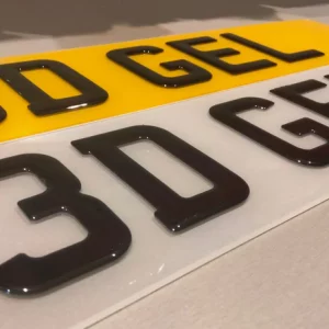 A close-up shot of two 3D Gel number plates side-by-side, one with a white background and one with a yellow background, featuring the raised, glossy characters "3D GEL".