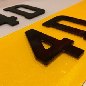 A close-up of a pair of 4D number plates, one with a white background and one with a yellow background, featuring large, raised black acrylic "4D" characters.