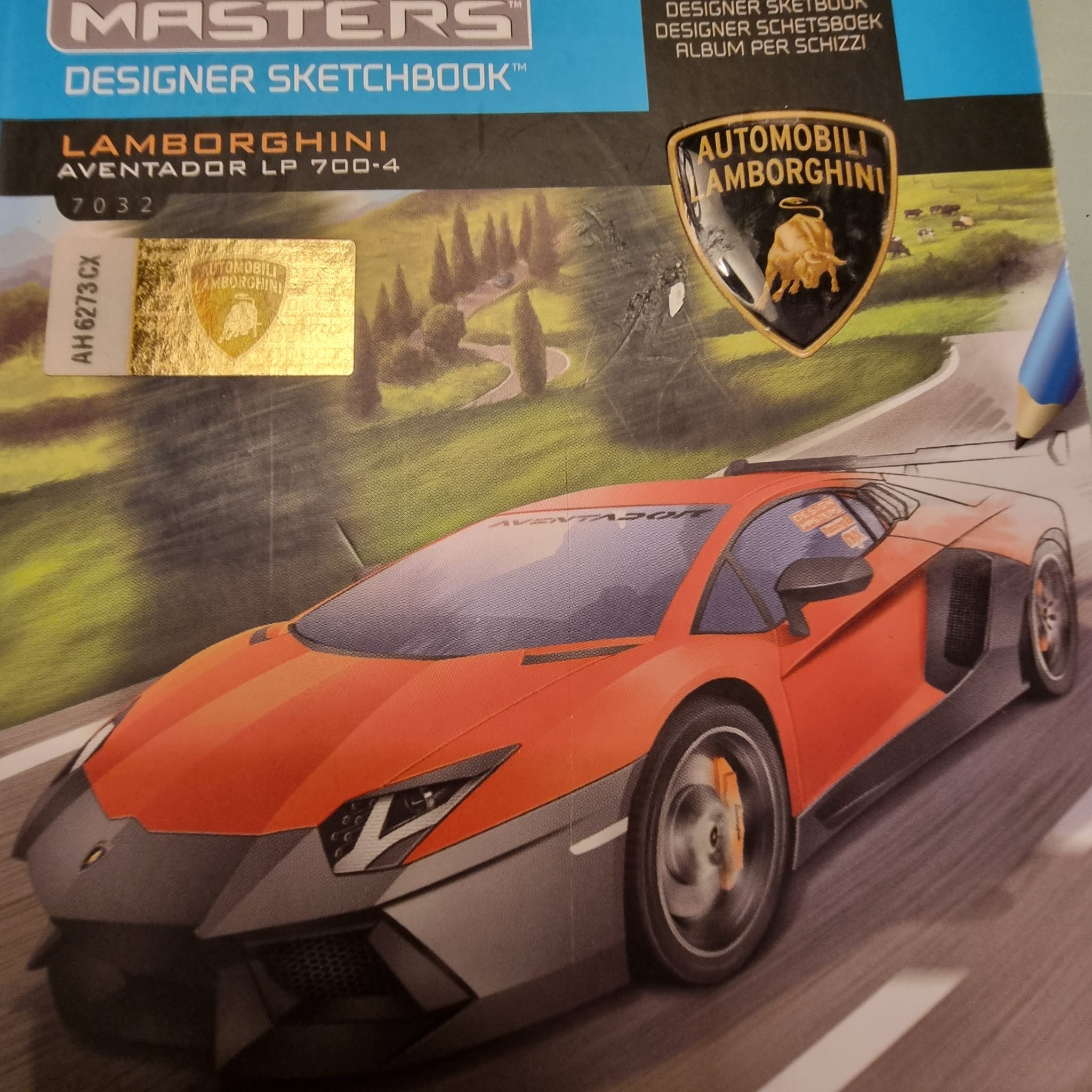 A "Design Masters" Lamborghini Aventador LP 700-4 sketchbook cover, featuring an orange car illustration, a gold hologram authenticity sticker, and the Lamborghini crest.