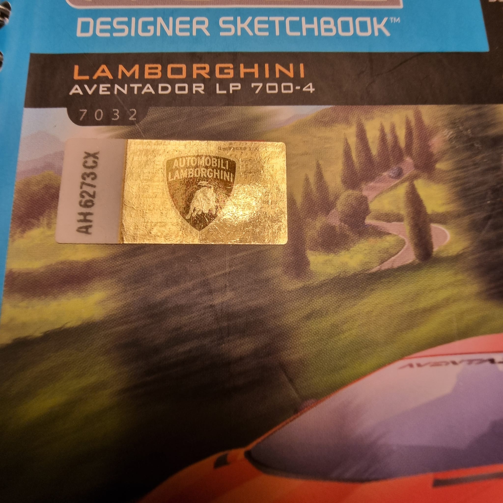 Close-up of an official gold Lamborghini hologram sticker with a serial number on a design book cover.